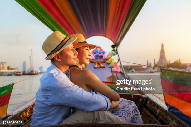 attractive mixed race romantic couple sightseeing wat arun in chao phraya river with longtail boat tour along the river in bangkok, thailand - longtail boat stock pictures, royalty-free photos & images