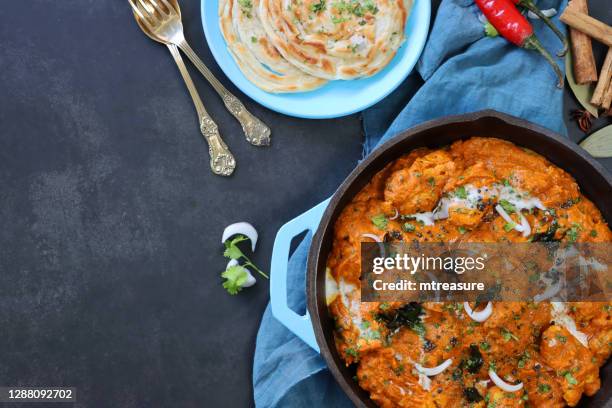 image of turquoise blue cooking pan filled with butter chicken / tikka curry, large chunks of chicken breast meat in curry sauce with garnish of red onion slices and mustard seeds, lachha paratha (layered flatbread), copy space, elevated view - masala stock pictures, royalty-free photos & images