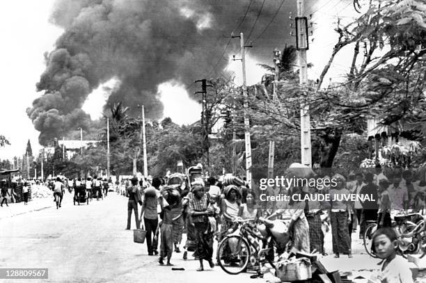 Cambodian inhabitants wait in a street of Phnom Penh, 17 April 1975 as the gasoline depot burns before the Khmer Rouge enter the capital and...