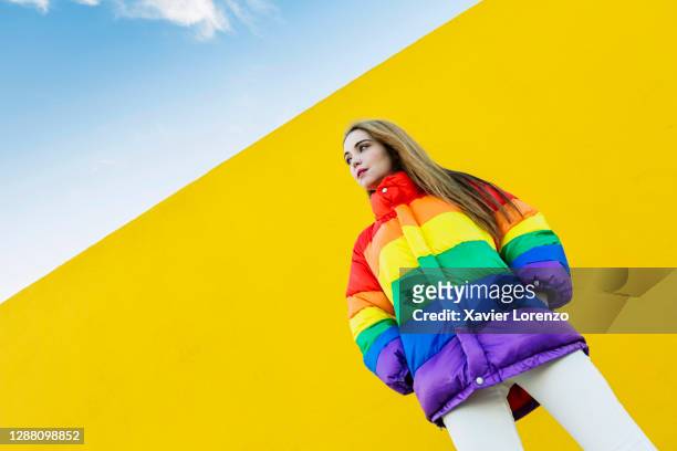 woman with colorful jacket in front of yellow wall - multi colored coat stock pictures, royalty-free photos & images