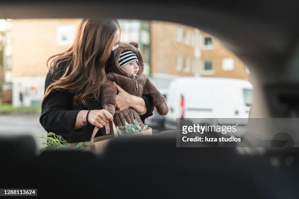 mother with face mask carrying baby and groceries - car scandinavia stock pictures, royalty-free photos & images