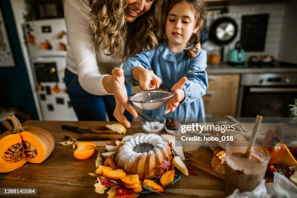 mutter und tochter bestreuen puderzucker auf kuchen - persimone stock-fotos und bilder