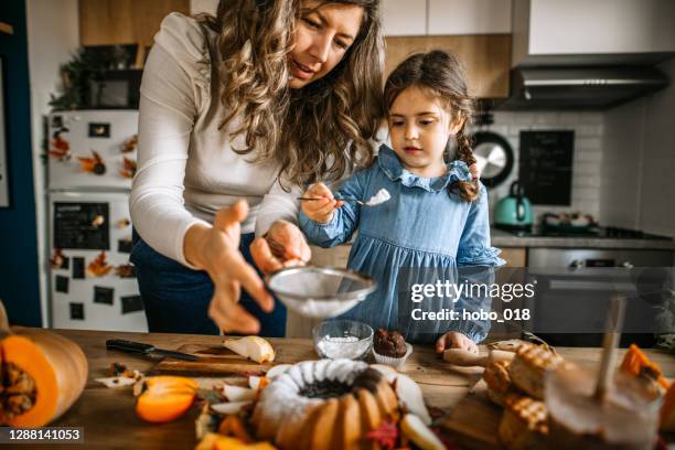 mother and daughter in kitchen dusting cake with powdered sugar - girl baking stock pictures, royalty-free photos & images