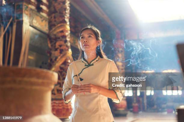 asiatische frau in traditioneller kleidung beten mit joss stöcken an buddhistischen tempel - religiöse opfergabe stock-fotos und bilder