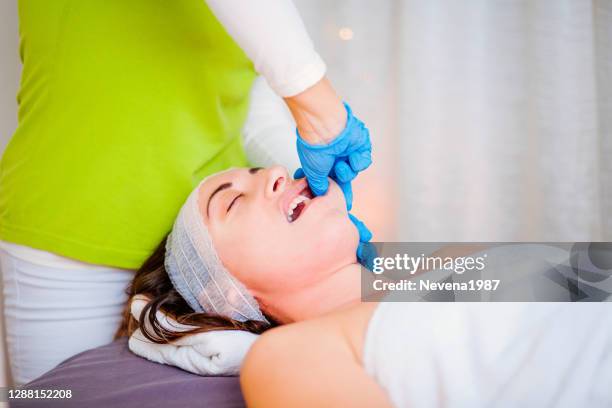 de fysiotherapeut maakt gezichtsmassage die aan de kaak van de vrouw in schoonheidskliniek werkt - human jaw bone stockfoto's en -beelden