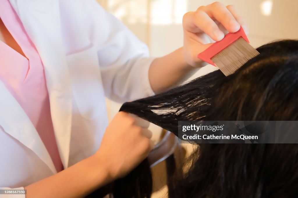 Mixed-race female school nurse holding small wire comb completes a lice check hair examination on a student