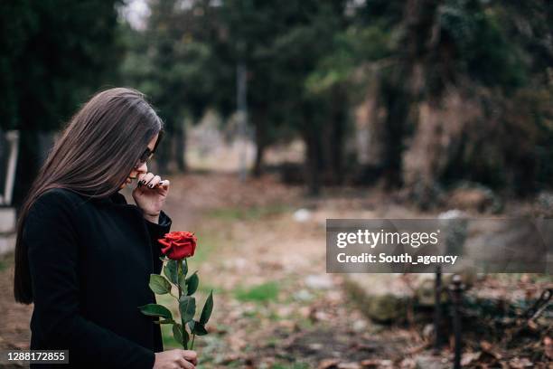 joven mujer llora en un cementerio sosteniendo rosa - viuda fotografías e imágenes de stock