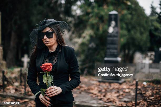 sad woman carries flowers to a grave in a cemetery - rosa rock stock pictures, royalty-free photos & images