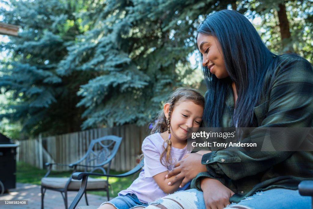 Young woman and small girl sitting on bench in back yard