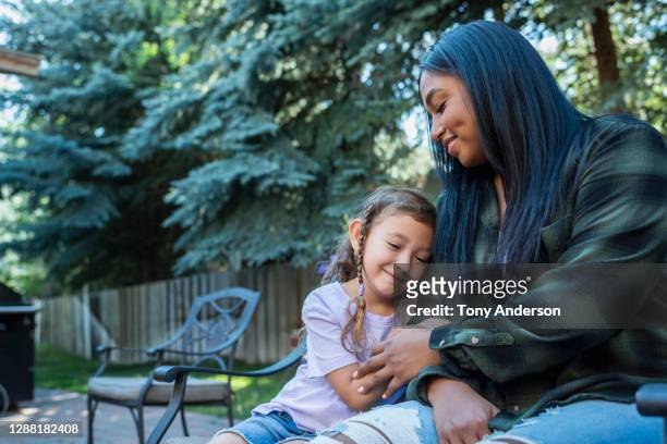 young woman and small girl sitting on bench in back yard - nanny stock pictures, royalty-free photos & images
