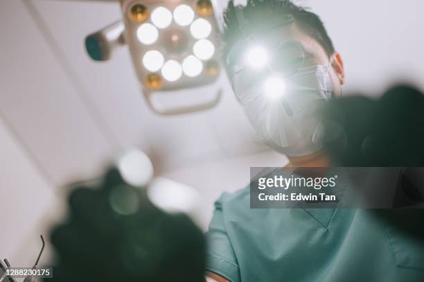 endodontiste chinois asiatique de dentiste chinois avec des loupes et la lumière regardant d’en haut au patient - roulette photos et images de collection