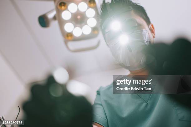 asian chinese male dentist  endodontist with magnifying glasses and light looking from above at patient - asia surgery stock pictures, royalty-free photos & images