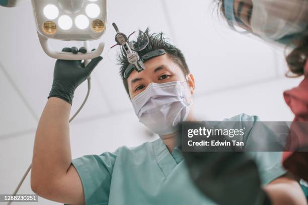asiatische chinesische männliche zahnarzt endodontist mit lupe und licht von oben auf den patienten schauen - dental hygienist stock-fotos und bilder