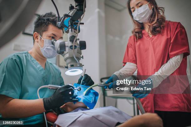 asiatische chinesische männliche zahnarzt blick durch mikroskop auf patientenzähne in zahnarztpraxis wurzelkanal behandlung - root canal procedure stock-fotos und bilder