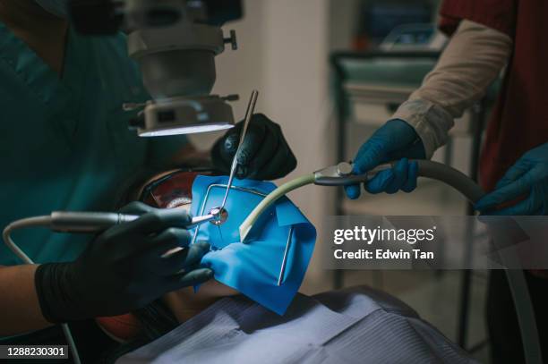 asiatische chinesische männliche zahnarzt blick durch mikroskop auf patientenzähne in zahnarztpraxis wurzelkanal behandlung - root canal procedure stock-fotos und bilder