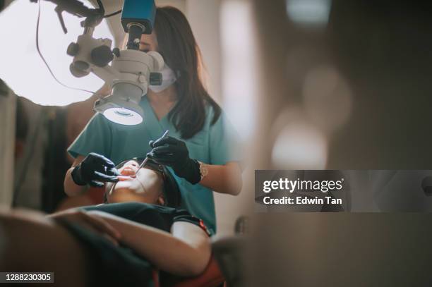 asiatico dentista cinese che guarda attraverso il microscopio sui denti del paziente nell'ufficio del dentista - ortodonzia foto e immagini stock
