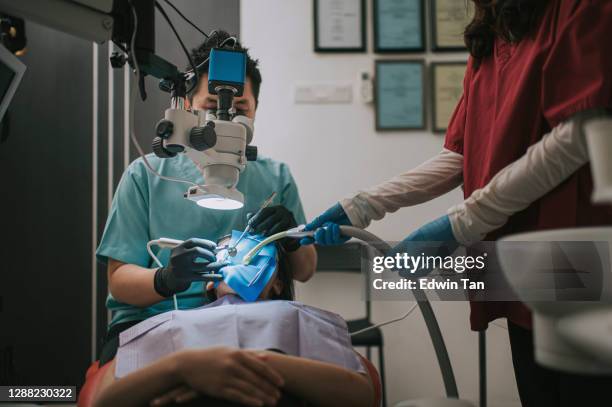 asian chinese male dentist looking through microscope on patient's teeth in dentist's office root canal treatment - root canal procedure stock pictures, royalty-free photos & images