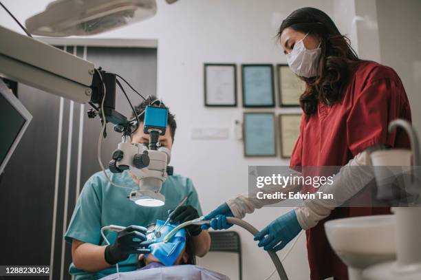 asiatische chinesische männliche zahnarzt blick durch mikroskop auf patientenzähne in zahnarztpraxis wurzelkanal behandlung - root canal procedure stock-fotos und bilder