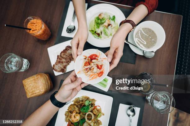 directly above view of young asian couple enjoying freshly served thai fusion cuisine, sharing food and passing a papaya salad bowl over the dining table in a thai restaurant - fusion food stock pictures, royalty-free photos & images