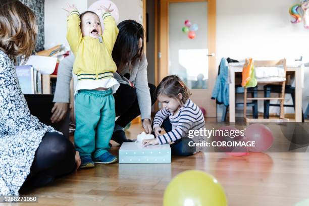 little girl opening her birthday present together with her family - stock photo - kids birthday present stock pictures, royalty-free photos & images