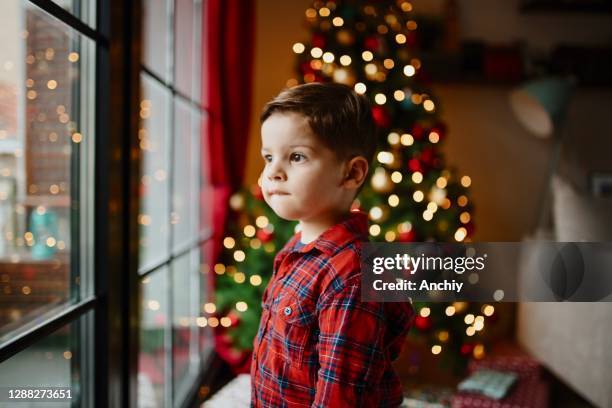 piccolo ragazzo carino che guarda attraverso la finestra e aspetta babbo natale - before christmas foto e immagini stock