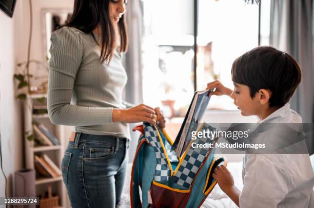 young boy putting his notebook in the backpack, the mother is helping him - child rucksack stock pictures, royalty-free photos & images