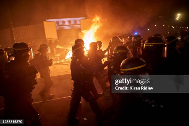 French Riot Police walk past a fire towards protesters at Place de la Bastille as demonstrations against the French Government's Global Security Law...