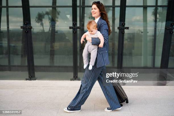 side view of a happy mother carrying her baby and dragging the suitcase - supermom stock pictures, royalty-free photos & images