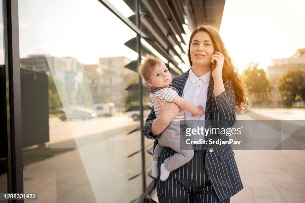 赤ちゃんを抱きながら外で電話で話すビジネスウーマン - supermom ストックフォトと画像