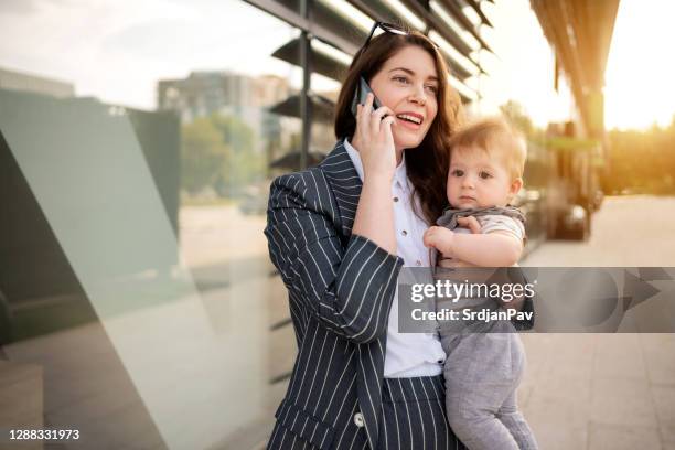 businesswoman talking on the phone while carrying her baby outdoor - baby superhero stock pictures, royalty-free photos & images