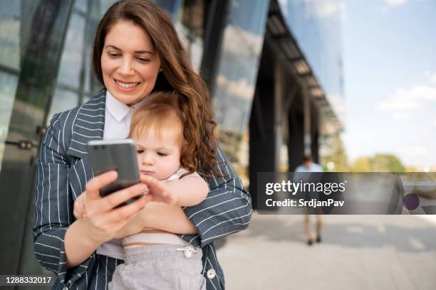 彼女のかわいい男の子を運びながら、スマートフォンとテキストメッセージを保持している若い母親 - supermom ストックフォトと画像