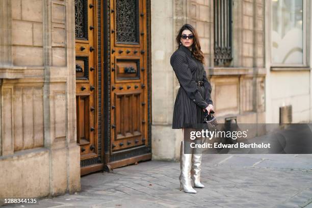 Sara Carnicella wears sunglasses from Jimmy Fairly, a black / gray striped dress with shirt collar, shoulder pads and a pleated lower part from Seyit...