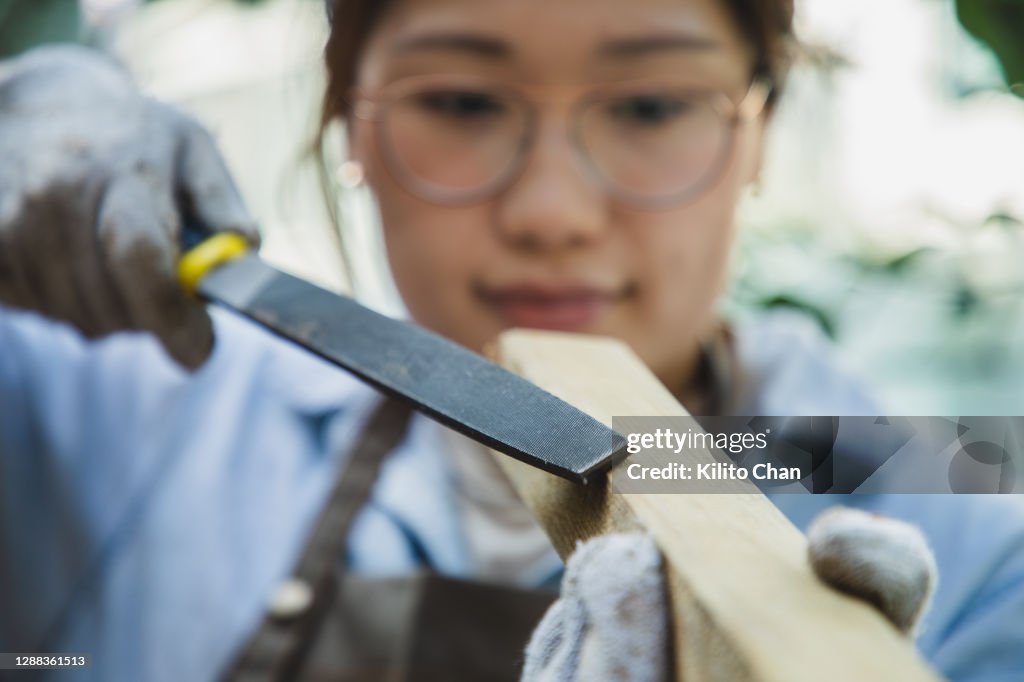 Asian woman shaping wood with rasp