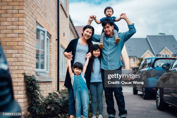 cheerful young asian family standing in front of house - settler stock-fotos und bilder