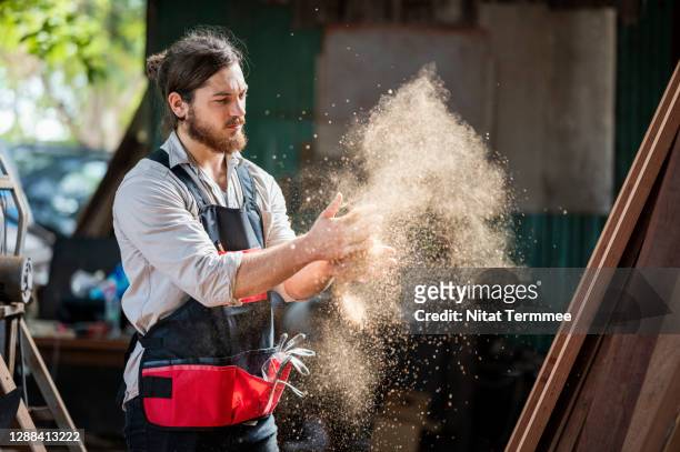 woodworker cleaning wood dust from his gloves by clapping hands in the wood workshop. - artisan food stock-fotos und bilder