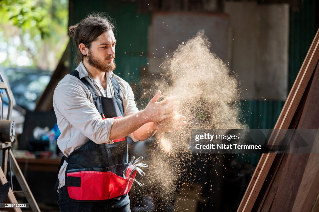 Woodworker cleaning wood dust from his gloves by clapping hands in the wood workshop.
