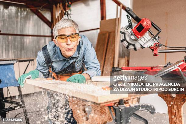 la carpintera madura corta un pedazo de tabla con una sierra de inglete. - mitra fotografías e imágenes de stock