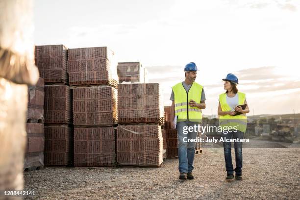 uomo e donna, i colleghi edili mangiano spuntini e chiacchierano amichevolmente dopo un'estenuante giornata di lavoro al tramonto vicino ai mattoni - construction material foto e immagini stock