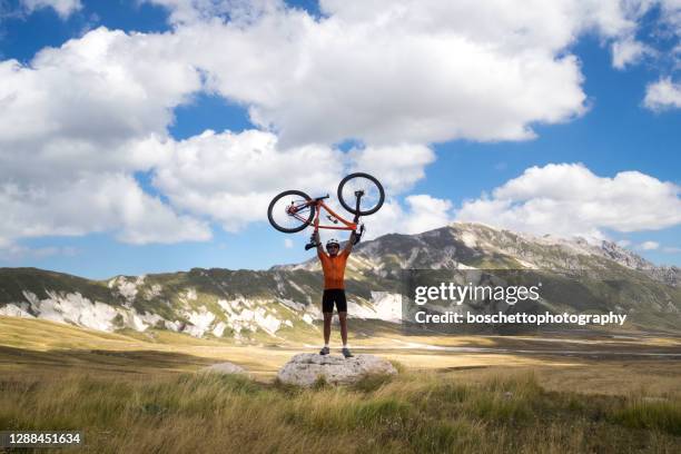 mountain biker holding bike above head; scenics on background - bike winning imagens e fotografias de stock