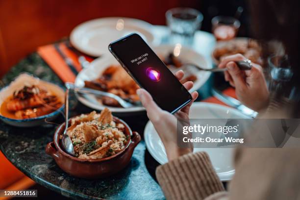 young woman talking to a virtual assistant on smartphone - dinner program stock pictures, royalty-free photos & images