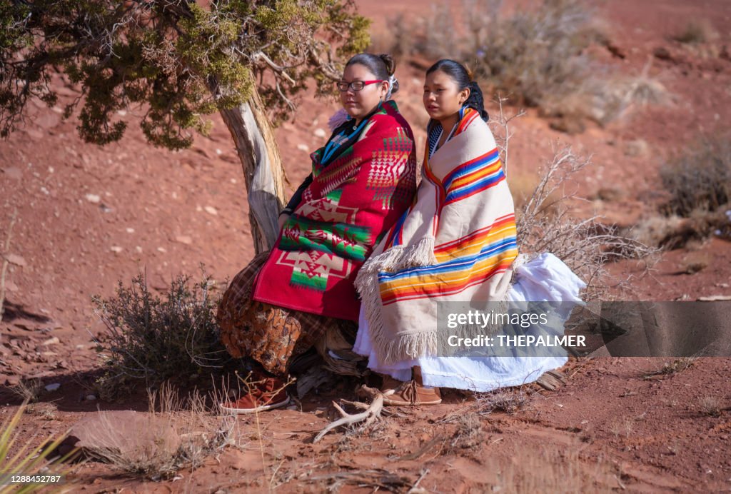 De zusters die van Navajo op de boomstam van een kleine cederboom in de Vallei van het Monument zitten - Arizona