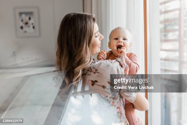 young woman mom with baby girl on hands near window at home - één ouder stockfoto's en -beelden