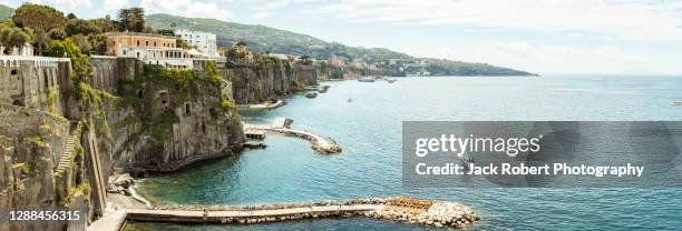 beautiful cliffside town overlooking the mediterranean sea with a yacht crusing by in sorrento, italy - sorrent stock-fotos und bilder