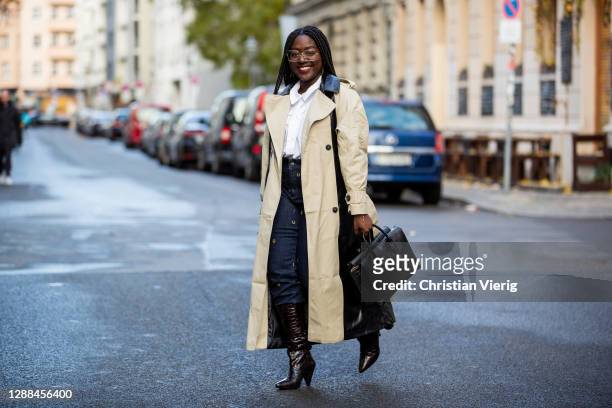 Lois Opoku is seen wearing two tone trench coat in black and beige, MCM bag, Rayban glasses, Samsoe Samsoe boots, blouse and denim jeans Munthe on...