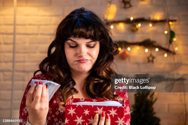 meisje in rode pyjama's opening kerstcadeau, krijgt ze beschermende gezichtsmaskers. zeer slechte x-massa cadeau. - negative emotion stockfoto's en -beelden