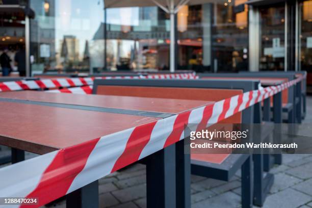 selected focus view at red and white caution tape restrict outdoor dining area of restaurant or cafe in düsseldorf, germany during lockdown by epidemic covid-19. - lockdown stock pictures, royalty-free photos & images