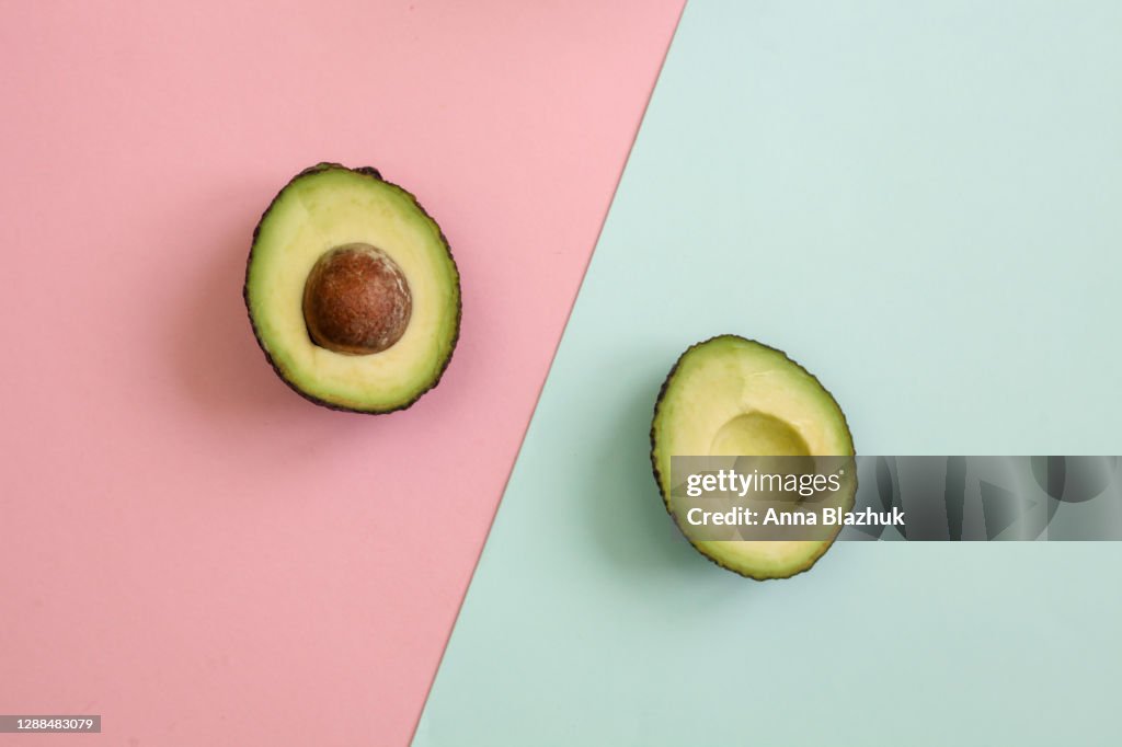 Flat lay of one halved fresh avocado over minimal pink background. Raw natural food.