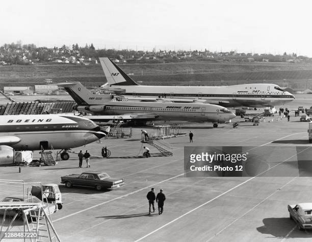 In the middle of the tarmac: Boeing 727-200 midsized three-engined jet aircraft. And in the background, a Boeing 747. 1969.