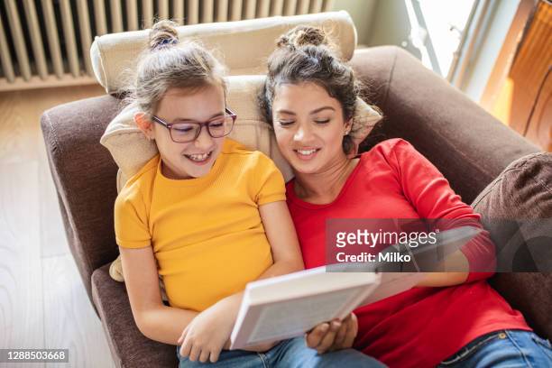 mother and daughter reading a book in living rom - class rom stock pictures, royalty-free photos & images