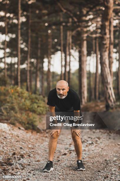 tired senior athlete man after running outdoors in forest. dehydration and breathlessness, dyspnea. problems with health of elderly people. - 息切れ ストックフォトと画像